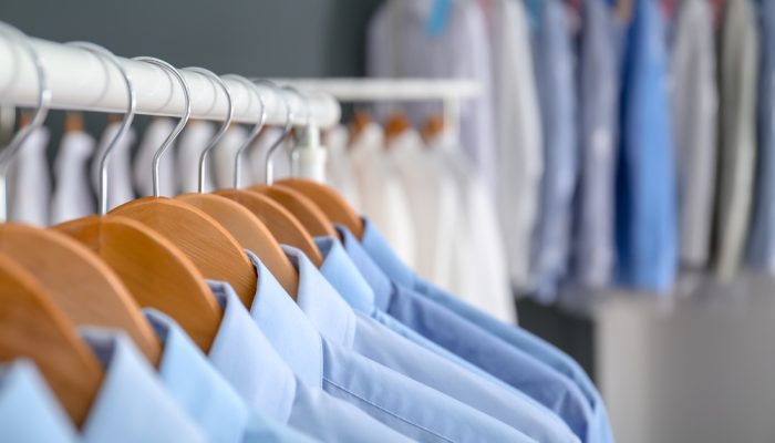 Rack with clean clothes on hangers after dry-cleaning indoors